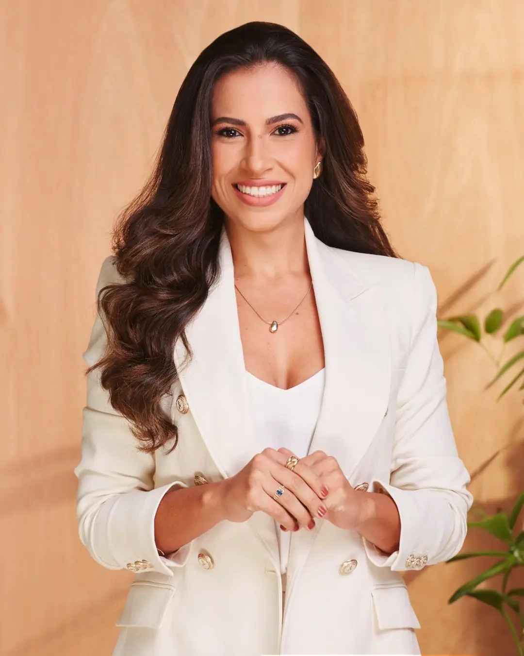 Gabriela de blazer branco, sorrindo, com as mãos unidas